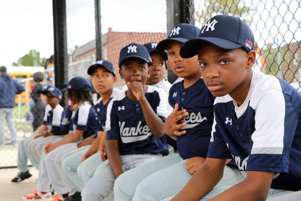 A group of young boys in navy blue and white Yankees baseball uniforms. They are all seated and looking at the camera.