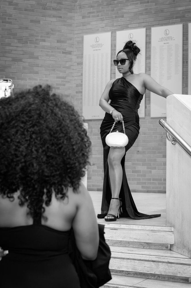 A woman in a black gown poses on some stairs.