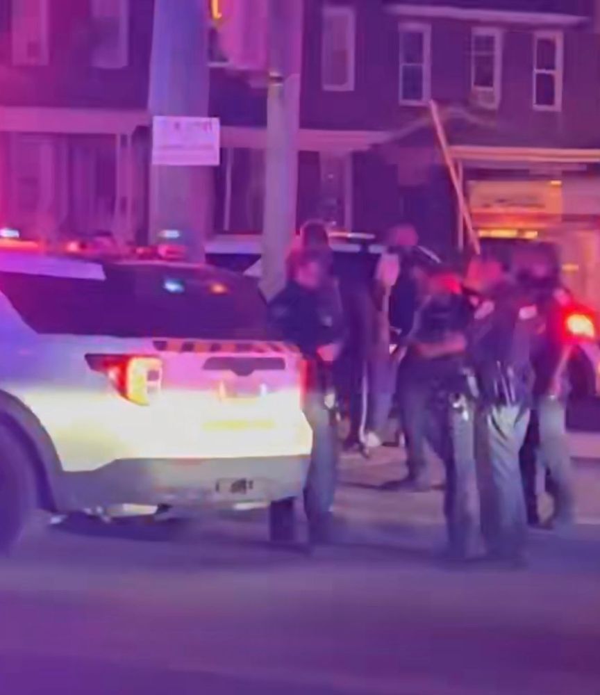 Screengrab of cell phone video showing the back of a Baltimore City Police Department video and officers standing nearby.