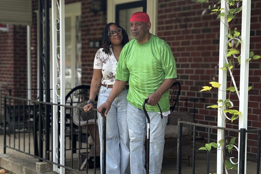 A younger woman and an older man stand on a porch together.