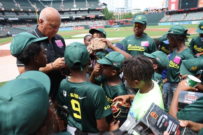 Young players in green and yellow gather around Cal Ripken Jr.