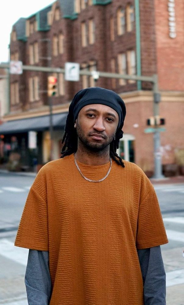 a man with brown skin stands at an intersection 