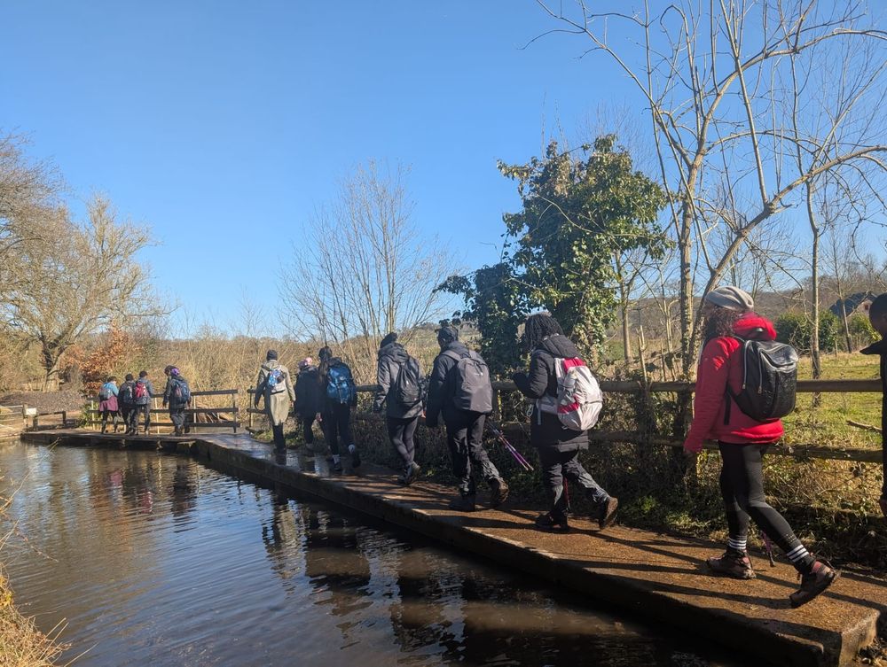 A group of Black women and men hikers walk along a river on a sunny day.
