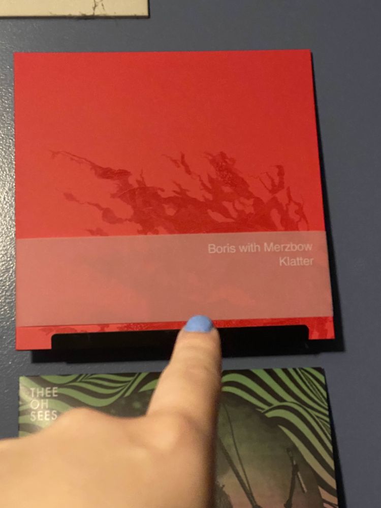 me pointing at my new vinyl, a copy of "Klatter", a collab between Boris and Merzbow. Its a red sleeve with a pretty texture, and a little white paper sleeve over top. My nails are painted a light blue color