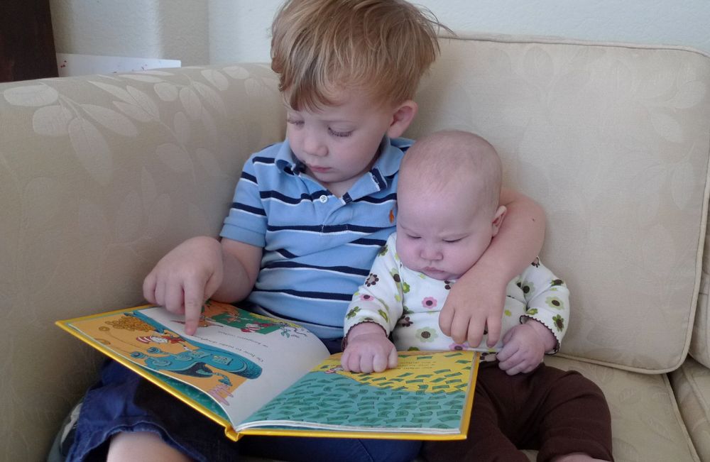 A baby girl and a toddler boy looking at a dr seuss book together. His arm is around her shoulder. It's pretty adorable.