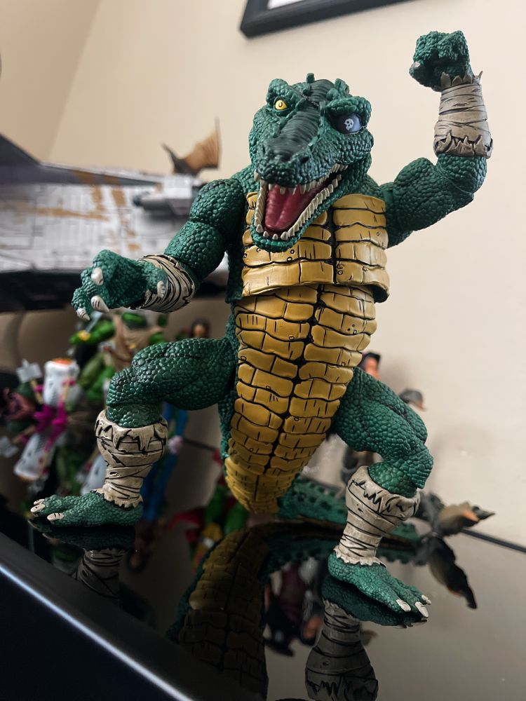 NECA Toys Leatherhead action figure from the Mirage TMNT line has a hinged jaw, and an eyepatch. He’s reaching out with one hand and raising his arm threateningly with the other.