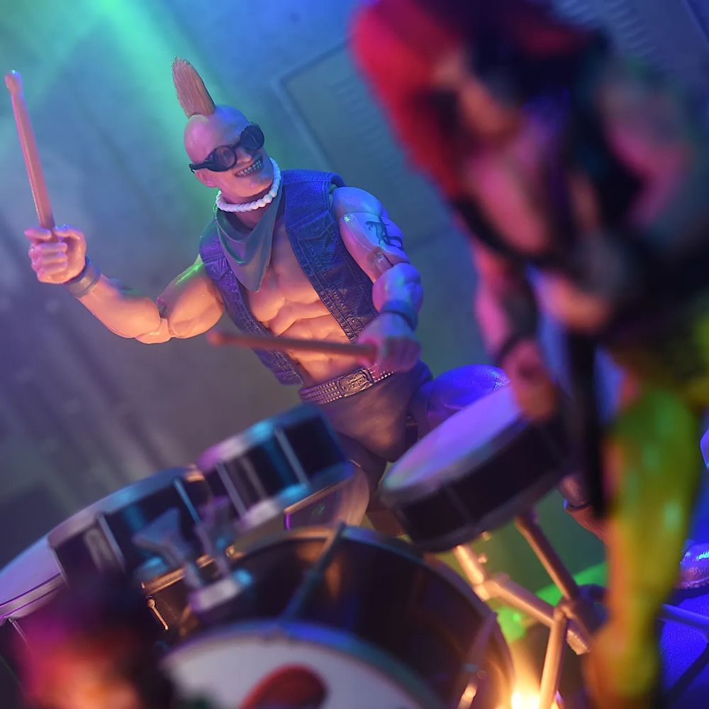 Dreadnok Buzzer in Mohawk and pearls cold slither costume playing drums.