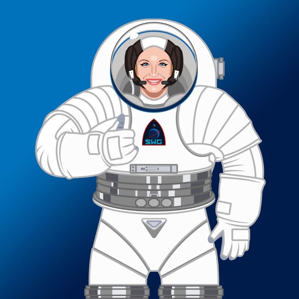A woman, wearing a hard torso spacesuit, gives a cheerful thumbs up.