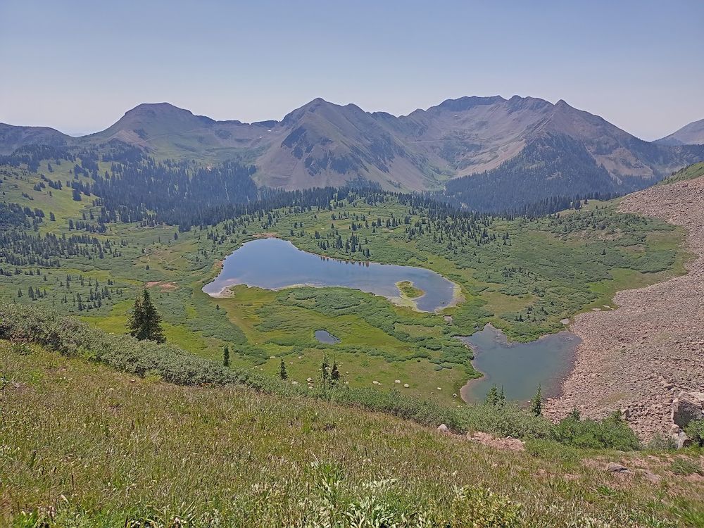 Looking down at Taylor Lake, a large lake surrounded by green meadows, pine trees, and a range of high peaks