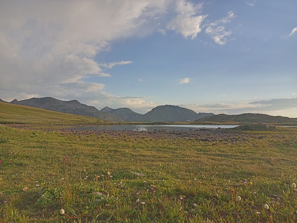 A high alpine meadow at sunrise with a shallow lake in the middle distance and the San Juans in the further distance