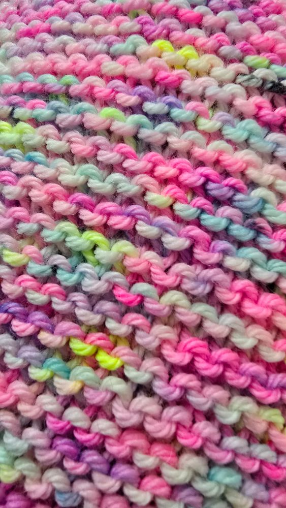 Hand-knit garter stitch with All The Gum yarn by Sock Obsession Yarns. It is hand-dyed yarn multicolored and speckled: hot pink, light pink, neon yellow, purple, sky blue, Robin's egg blue, green, and a few black speckles.