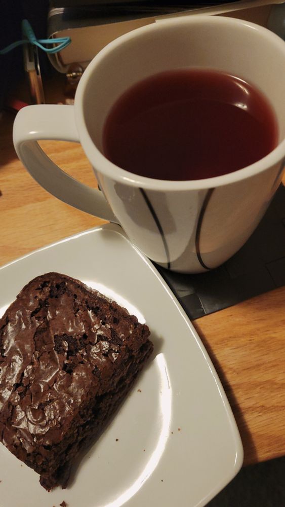 plate with a chocolate brownie and a mug with dark red tea on my coffee table