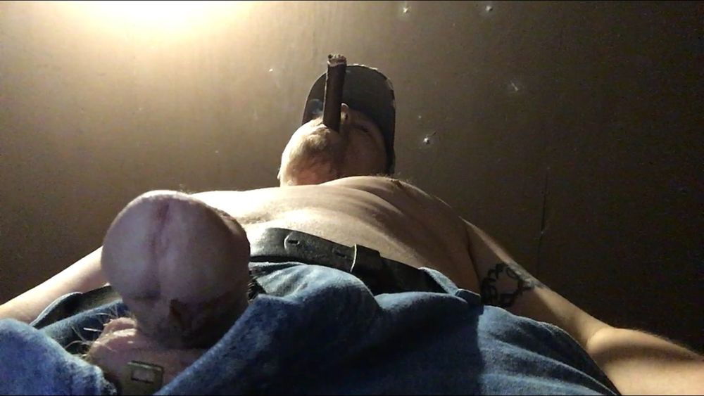 Craig Rauch is standing over you with his soft cock dangling from the hole in his unzipped jeans. The camera angle shows a view running up his body to his face where his cigar is hanging out of his mouth while he takes a pull on it.