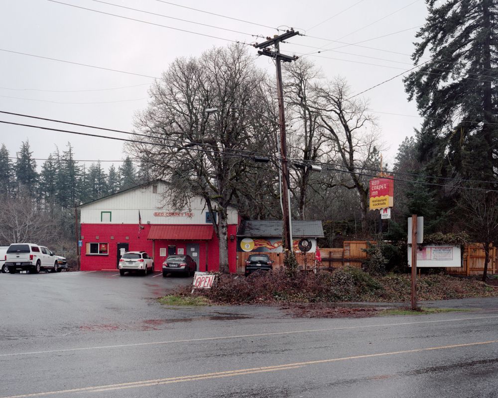 A restaurant called the Red Carpet Inn on a rainy day, surrounded by trees. An addition features a mural of flaming pool balls.