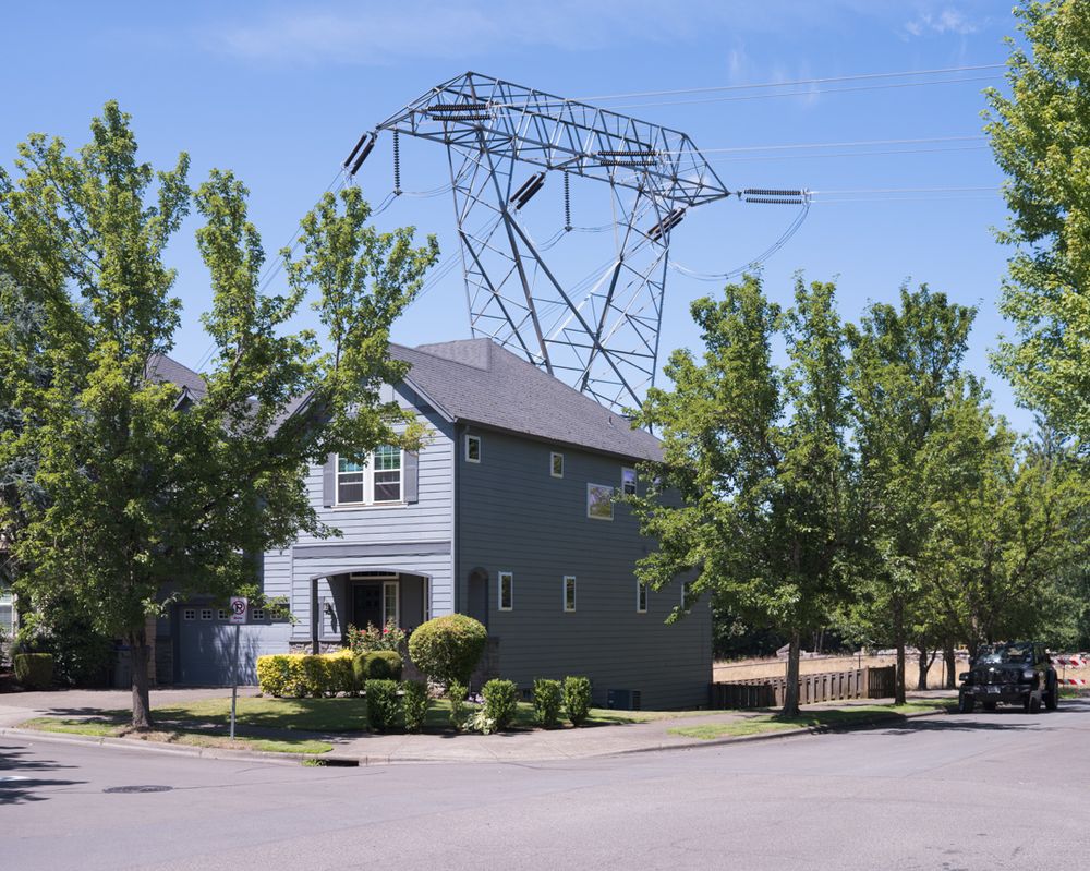 A high voltage electrical transmission line looms above a suburban house.
