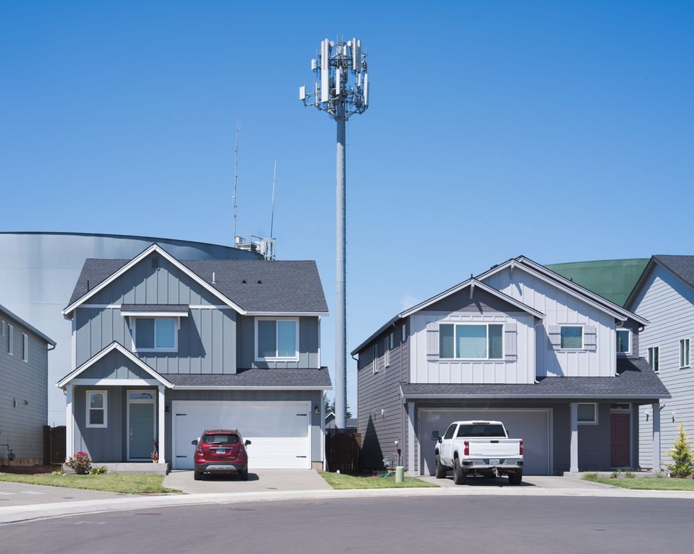 Two houses in the foreground have water tanks and a cellular tower immediately behind them.