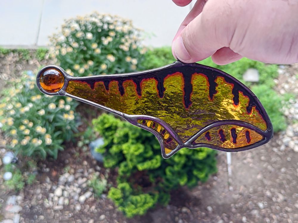 Same glass piece, but held against a backdrop of green vegetation.