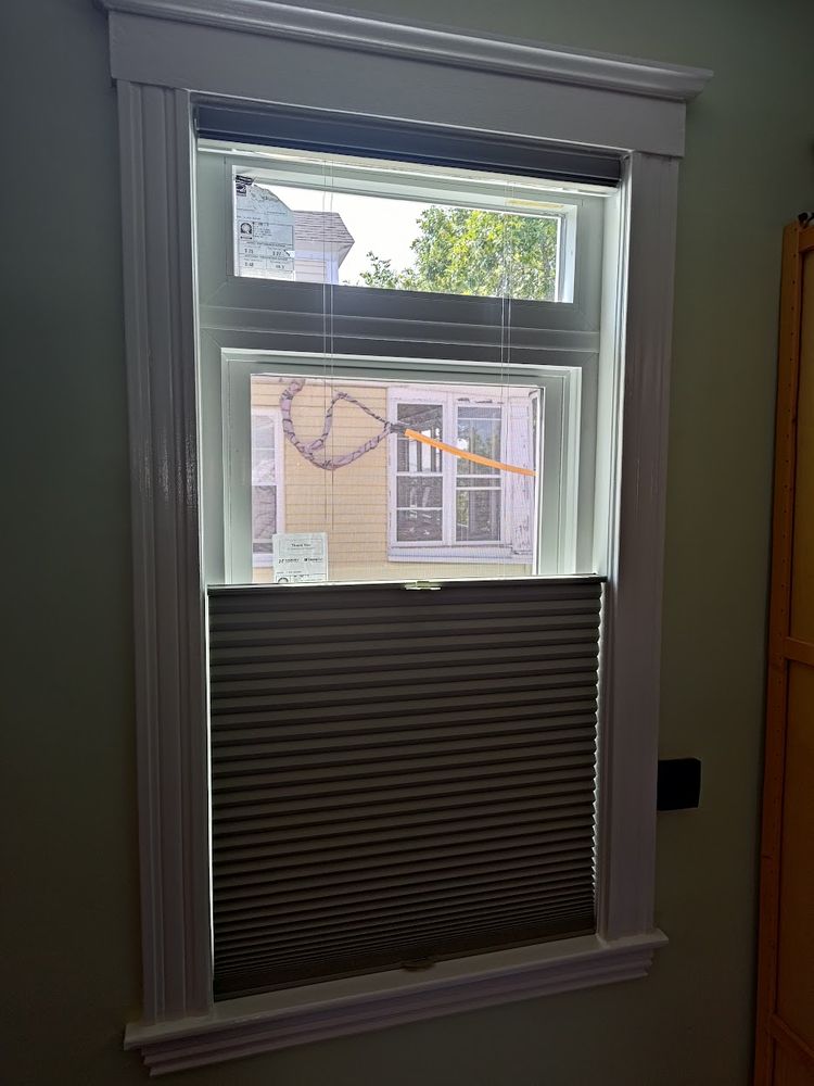 A single window with the shade pulled down enough to show the transom and part of of the upper operating sash.