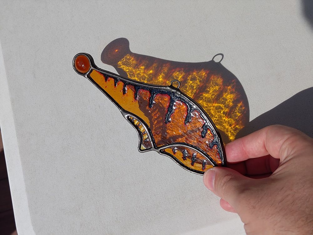Same glass piece, but held near a white table to show the colorful shadow of sunlight shining through it.