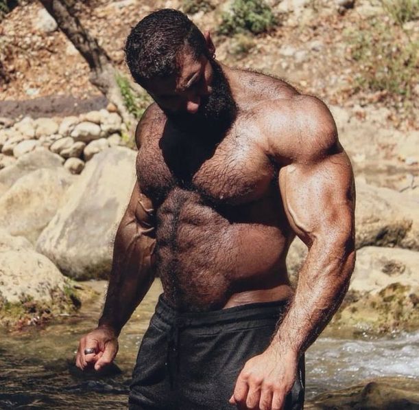 really large and hairy muscleman shirtless in a pond of water in the wild