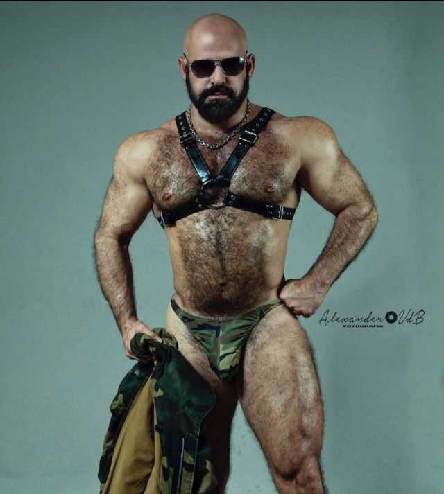 Muscled and hairy man wearing only a leather harness and a military speedo.