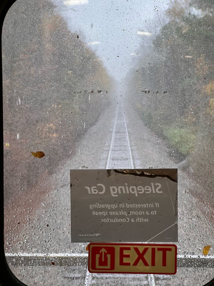 View out a rain speckled window at the tracks out the rear of a train 