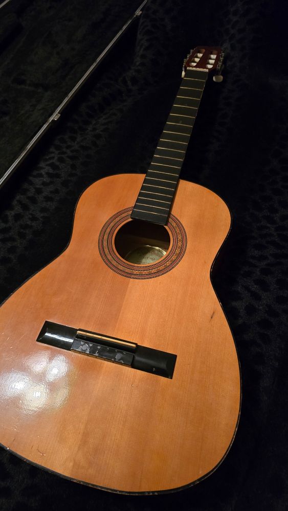 A classical guitar on a black panther-spotted blanket.