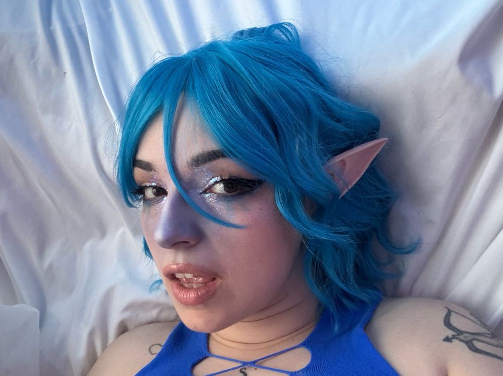 Learaypie wearing a blue wig and elf ears with glittery makeup. The elf ears look a little plastic but it’s okay she’s doing her best