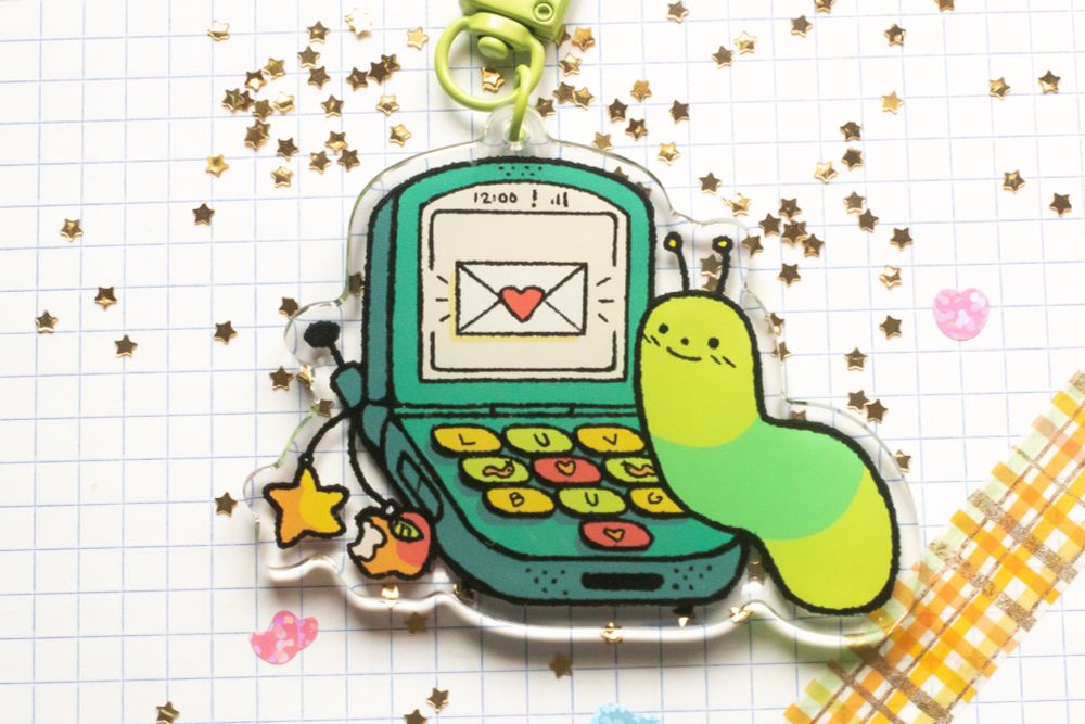 a picture of the luv bug keychain against a white grid background, surrounded by smaller glittery stickers and gold star glitter