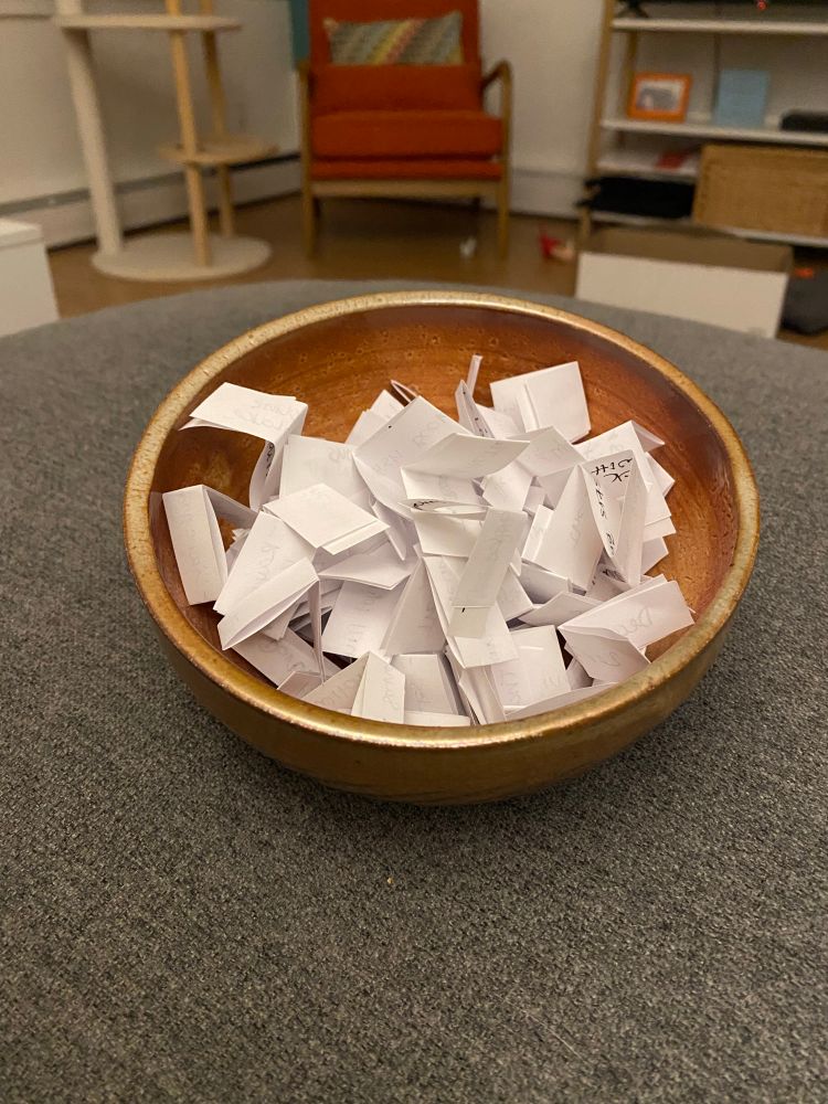 A small brown bowl containing folded pieces of paper with different book titles on them 