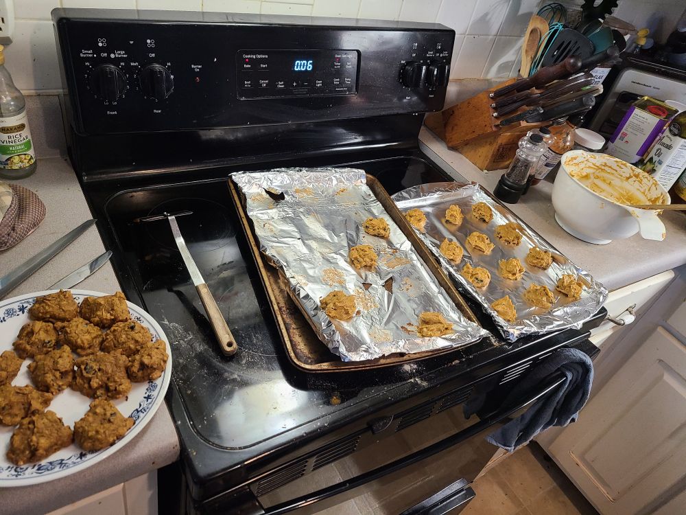 Sheets of raw cookies getting ready to be put in the oven. Off to the side is a finished plate of cookies