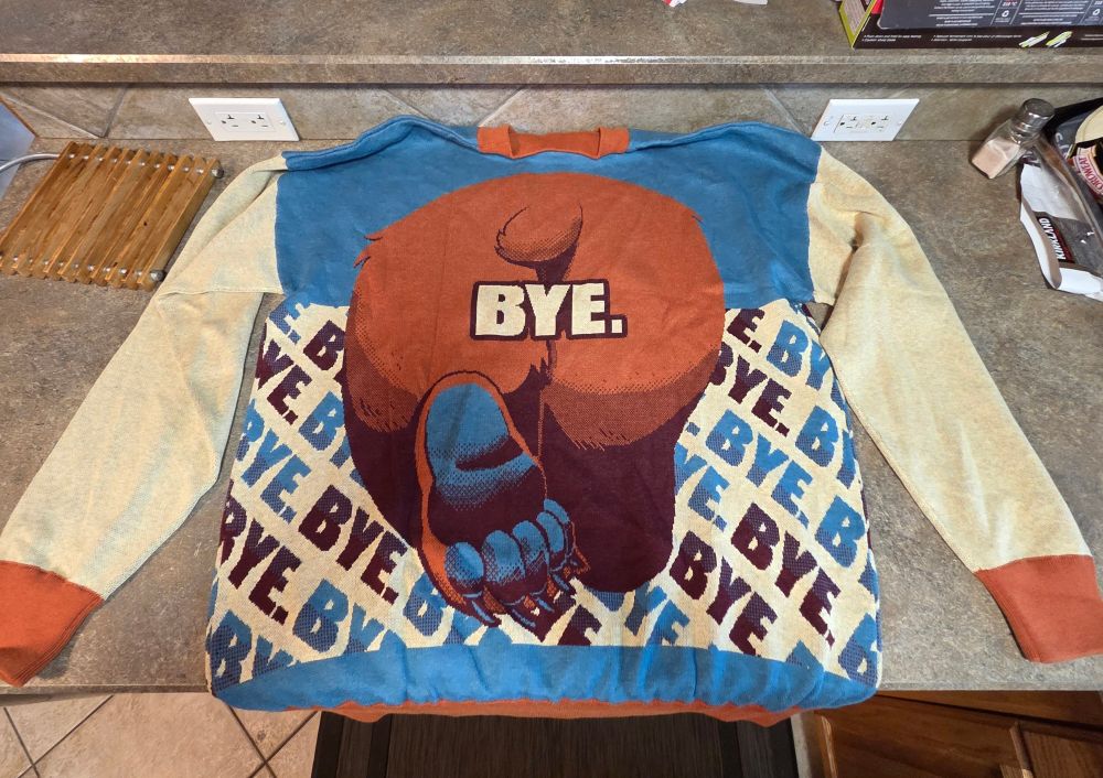 The back of the bear hoodie layed out on a counter it has a bears butt and paw walking away with bye under it.