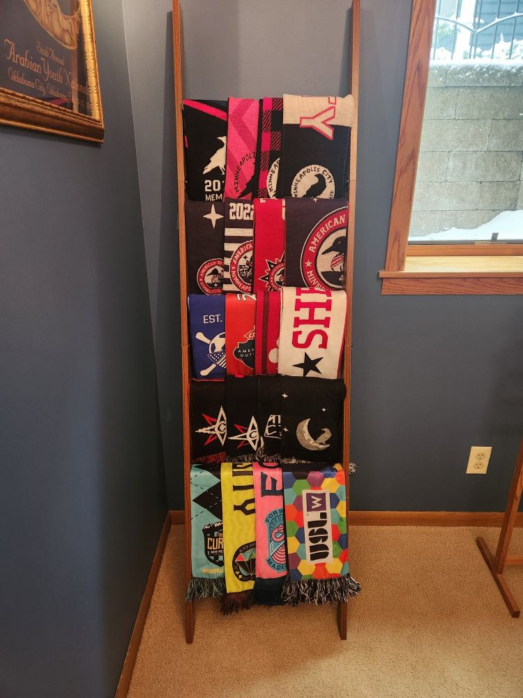 A blanket ladder covered in soccer scarves leaning against a blue wall