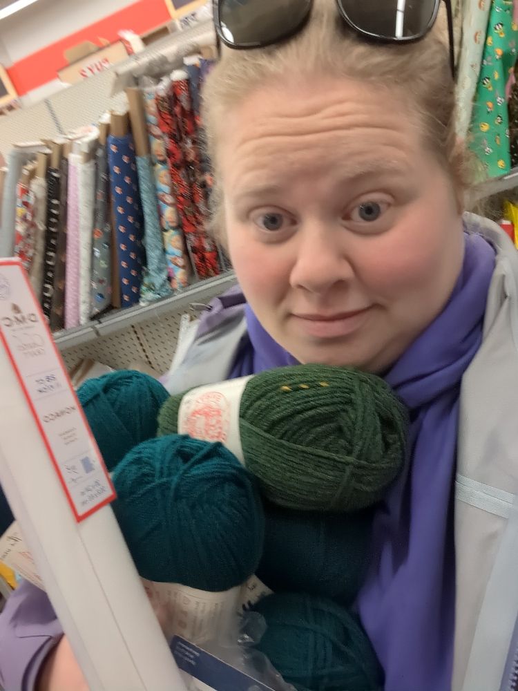 Selfie of me holding an armful of yarn and other craft supplies in the fabric aisle of a Michael's craft store