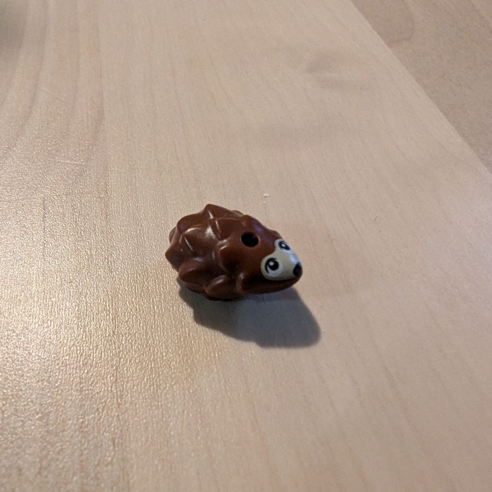A small brown Lego hedgehog piece with printed eyes and nose facing to the right