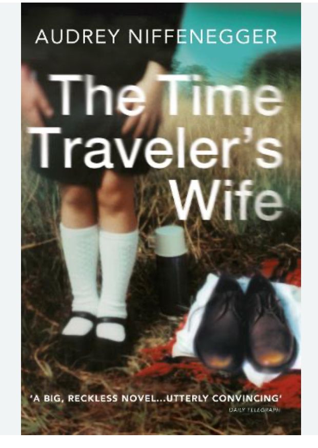Cover of book The Time Traveler’s Wife by Audrey Niffenegger - a girl’s leg to knees showing black strapped shoes and white knee socks and beside her a pair of worn brown man’s shoes on top of folded clothes. She is standing on a leafy area and has a small coffee flask just behind her
