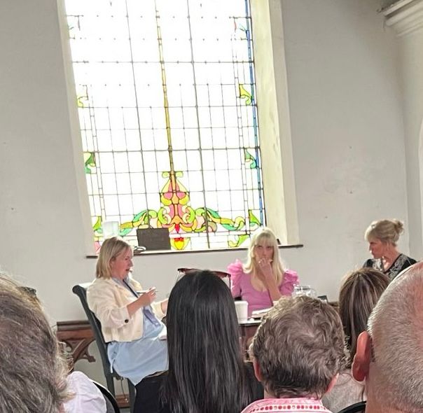 Some audience at bottom of photo looking up at interview with interviewer and two authors. Lovely stain glass long window behind the scene