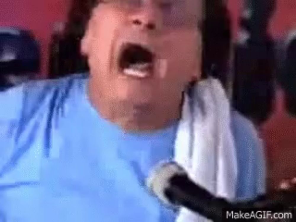 a man in a blue shirt is singing into a microphone