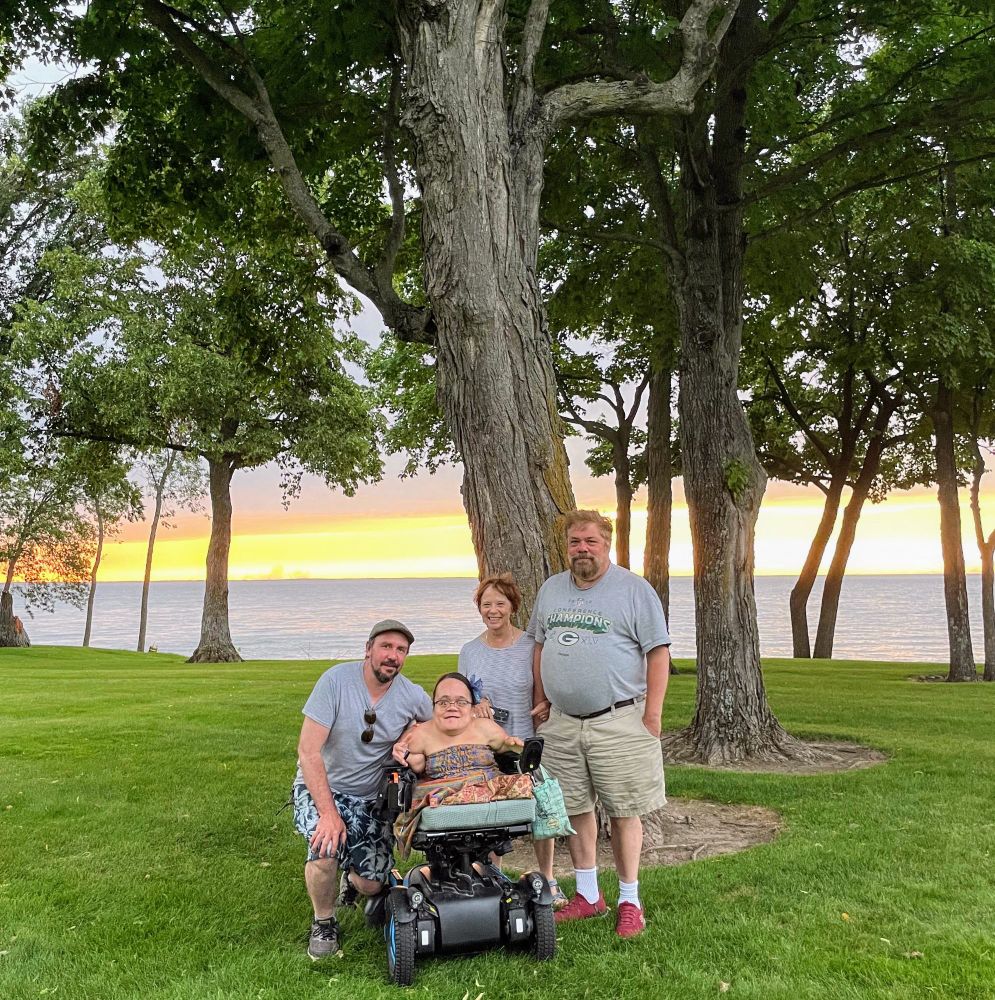 A picture of Gaelynn and her husband Paul smiling with Gaelynn's parents in front of Lake Mille Lacs at sunset.