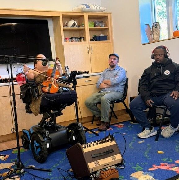 Gaelynn performs at the ARC of the Piedmont for disabled participants in their arts program. Paul is off to her left listening, as is one of the participants.
