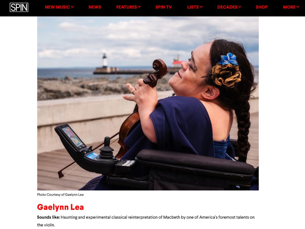 Image description: a picture of Gaelynn sitting on a boardwalk holding a violin. Her long dark hair is in a single braid with a blue and brown flower. She's wearing a blue dress and looking out over the water. There is a lighthouse in the distance. Above this picture are tabs for Spin Magazine, saying: 'SPIN NEW MUSIC NEWS FEATURES SPINTV LISTS DECADES SHOP MORE’. The description below her picture reads: “Photo Courtesy of Gaelynn Lea. Sounds like: Haunting and experimental classical reinterpretation of Macbeth by one of America’s foremost talents on the violin''