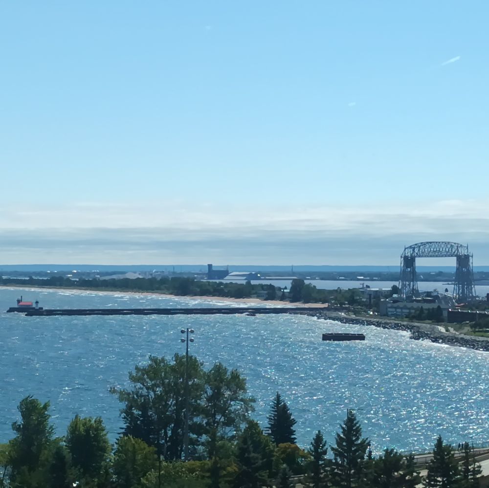 A picture of the Ariel Lift Bridge in Duluth, as well as the lighthouse. It is sunny and the water is glittering.