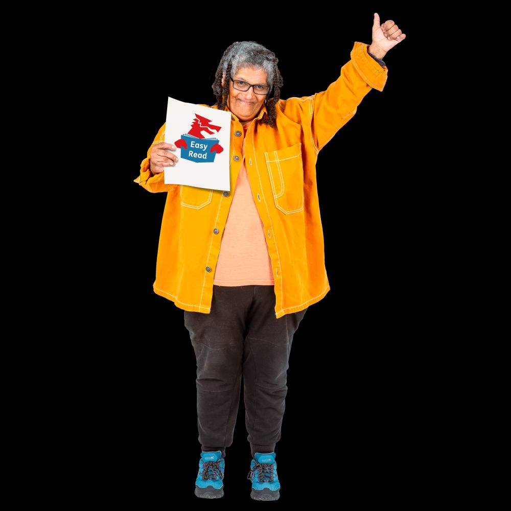 A smiling person holds a piece of paper with the Easy Read Wales logo. Their other hand is raised high, giving a thumbs up.