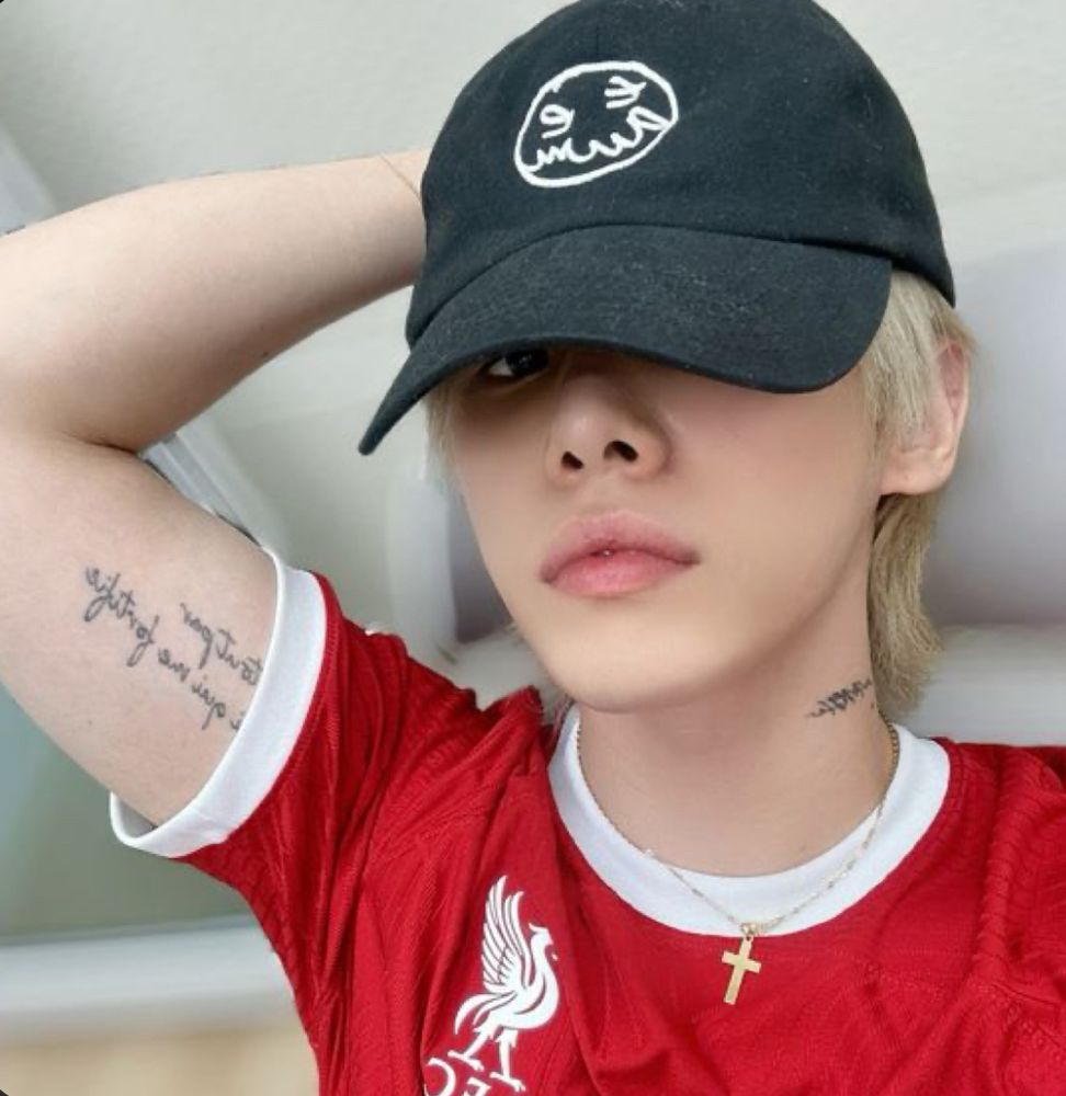 Xen from Omega X wearing a red shirt and black hat. His arm and neck tattoos are visible. 