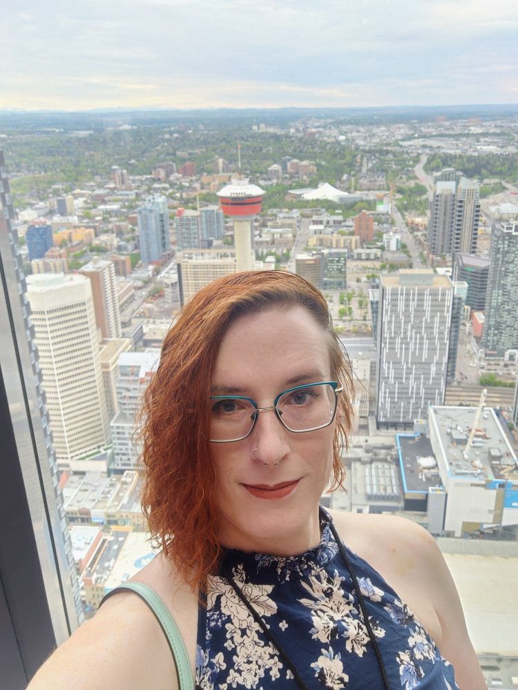 a red haired girl in a dark blue floral halter top with a cityscape in the window behind her