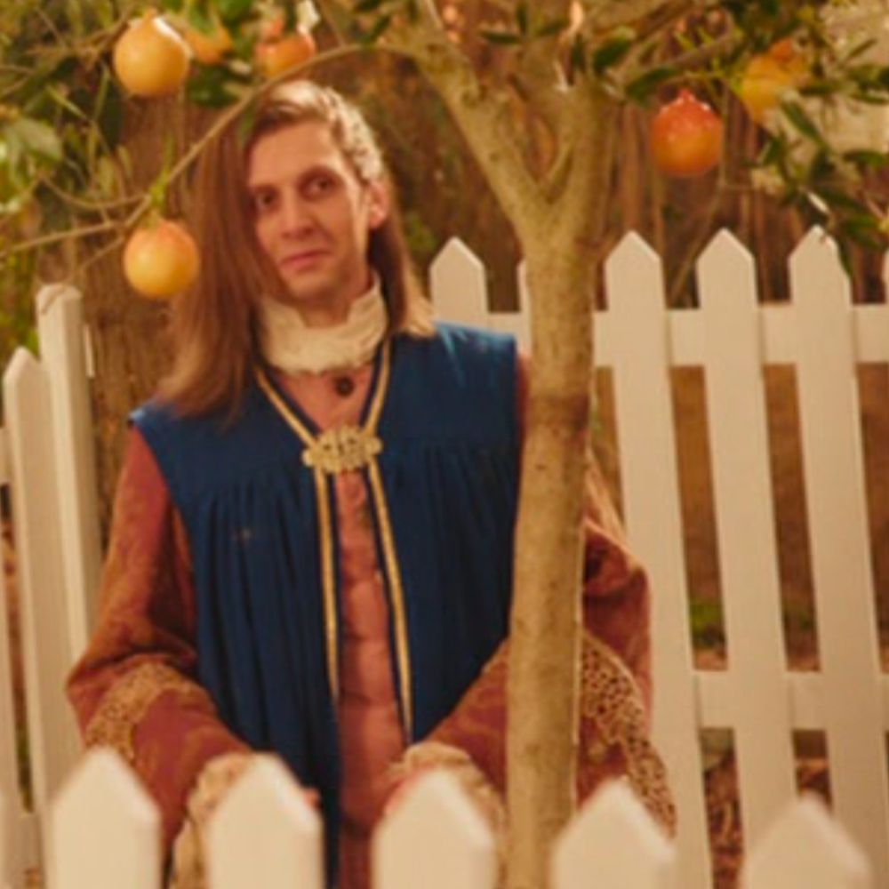 screenshot from the tv show yonderland, of scribe elder ho-tan.  she is standing beneath a pipplefruit tree, surrounded by a white picket fence, with a slight smile on her face
