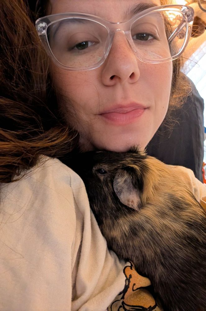 Woman in her mid-30s holding a guinea pig that is copper, brown, and black. 