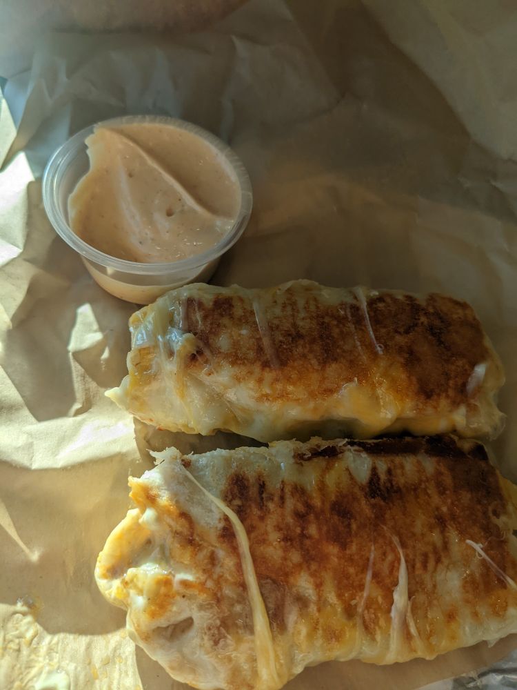 Two cute Lil mini burritos covered in melted cheese pictured next to dipping sauce 