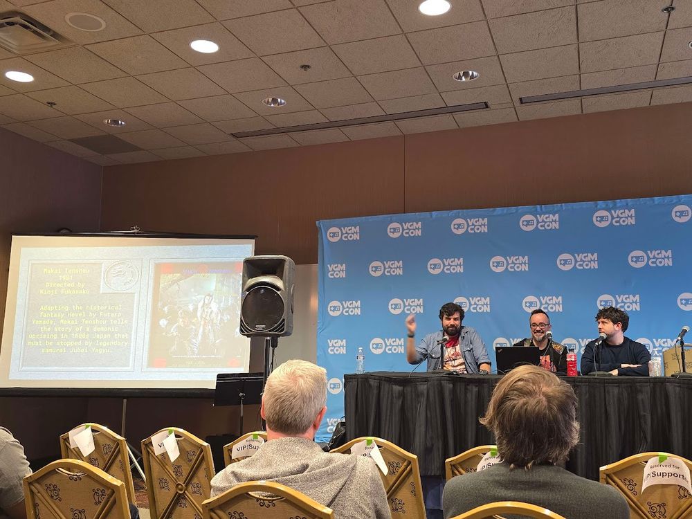 Matthew, Carlos, and Marty sitting on stage at VGM Con giving a panel next to a projector screen.
