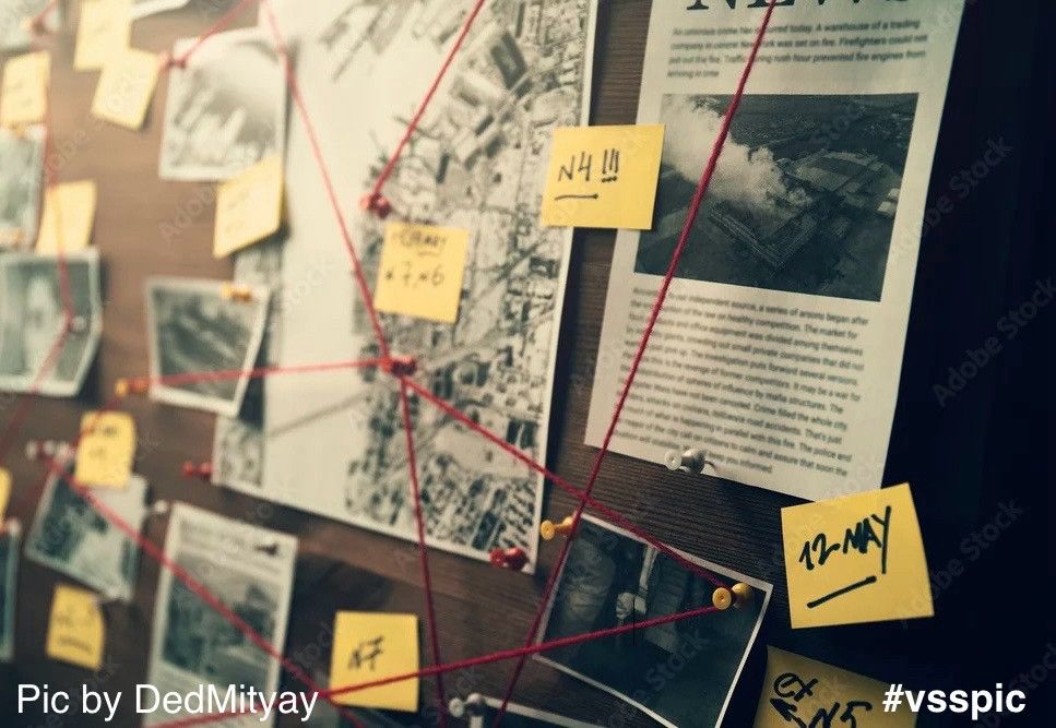 A corkboard holds a map and several pinned up photographs and articles, the pins linked by red string. Yellow post-its sprinkled throughout. A case awaits its breakthrough.